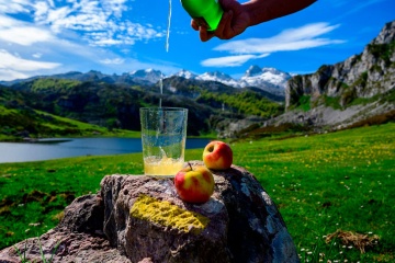 Pouring Asturian cider made from apples fermented from green bottles and high up with views of Lake Covadonga and the peaks of the Picos de Europa