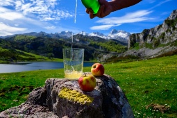 Einschenken von asturischem Apfelwein aus grünen Flaschen aus großer Höhe, hergestellt aus fermentierten Äpfeln, mit Blick auf den Covadonga-See und die Gipfel der Picos de Europa